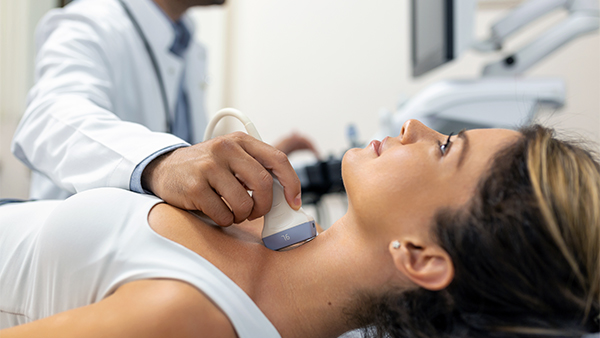 Healthcare professional performing a neck ultrasound on a woman lying down.